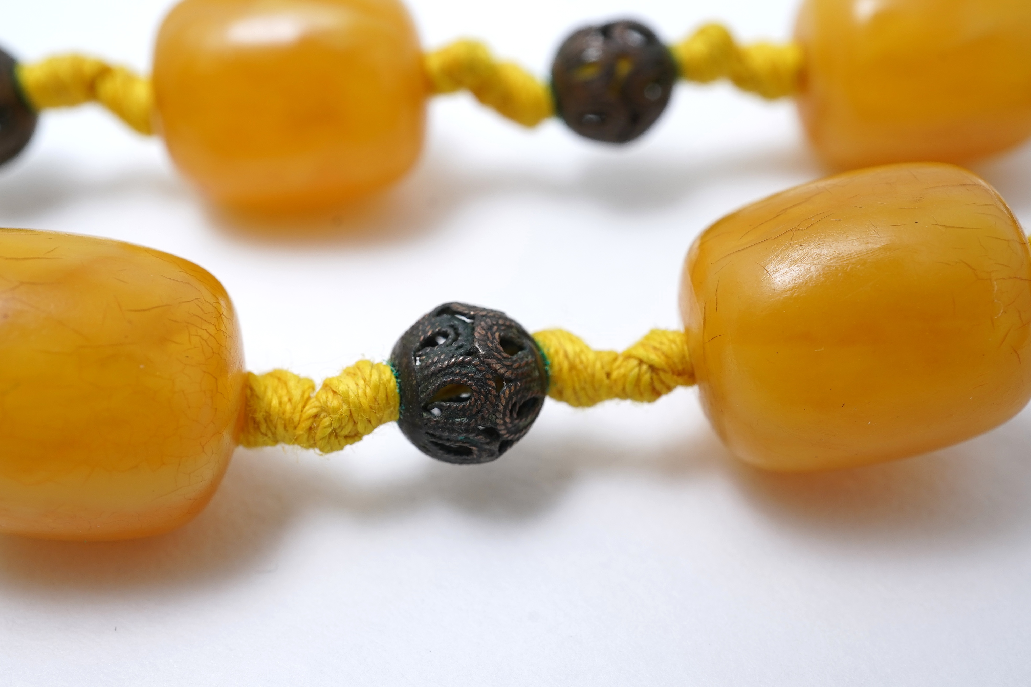 An amber necklace and carving, comprising: an amber necklace, composed of beads each measuring approximately 12 x 12 x 14mm, spaced by openwork metal beads, length 48cm; and an amber carving of a hawk on a rock, length 4
